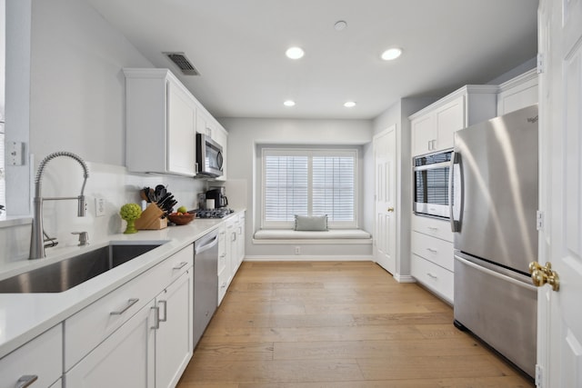 kitchen with visible vents, light wood finished floors, a sink, white cabinets, and appliances with stainless steel finishes