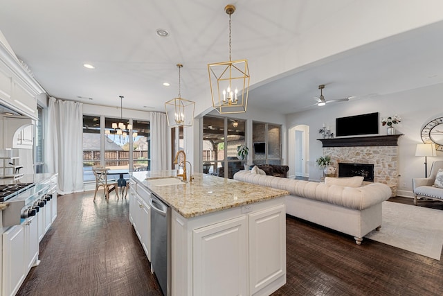 kitchen featuring a stone fireplace, ceiling fan with notable chandelier, arched walkways, white cabinets, and a sink