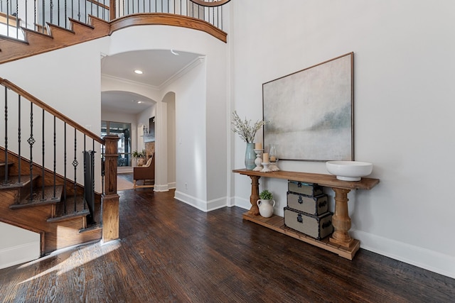 entryway with arched walkways, a towering ceiling, baseboards, and hardwood / wood-style floors