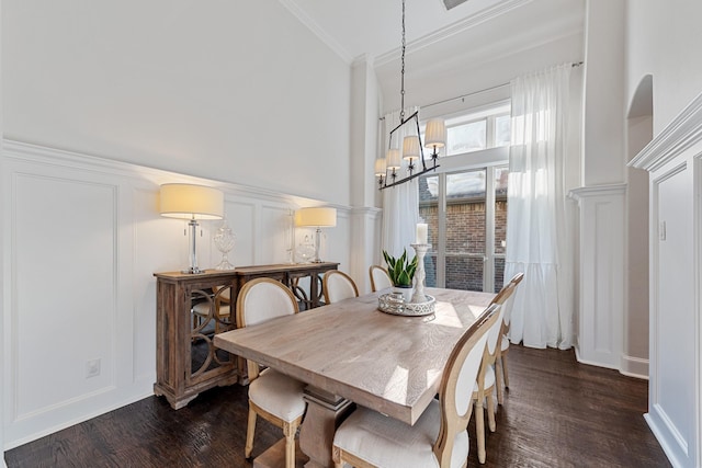 dining room featuring dark wood-style floors, ornamental molding, a towering ceiling, a decorative wall, and a notable chandelier