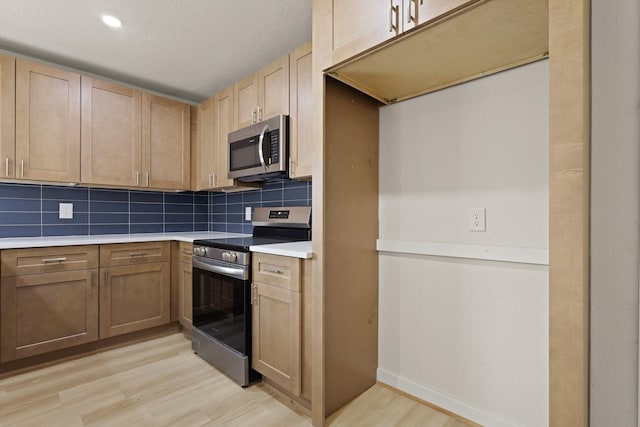 kitchen with light wood-type flooring, light brown cabinets, appliances with stainless steel finishes, light countertops, and decorative backsplash