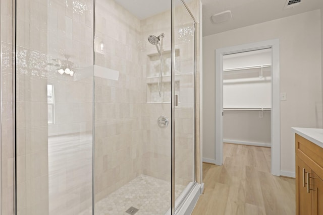 bathroom with vanity, a spacious closet, wood finished floors, and a stall shower