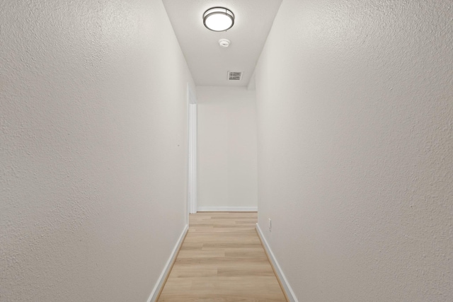 hall with light wood finished floors, visible vents, baseboards, and a textured wall