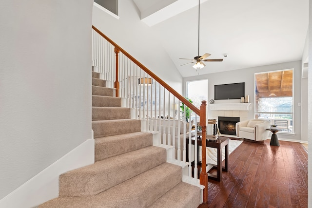 stairs featuring hardwood / wood-style floors, a tiled fireplace, a ceiling fan, and high vaulted ceiling