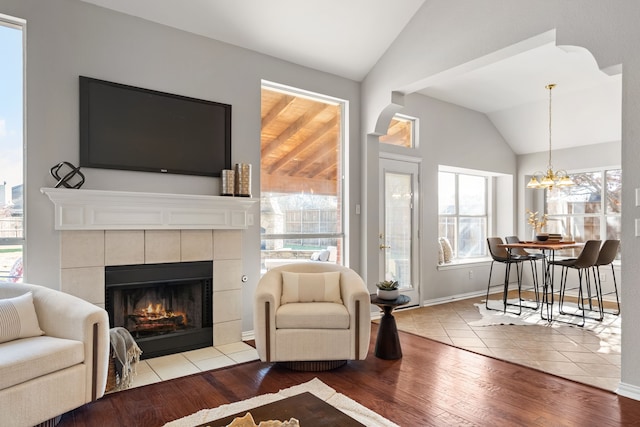 living room with wood finished floors, baseboards, a fireplace, lofted ceiling, and a chandelier