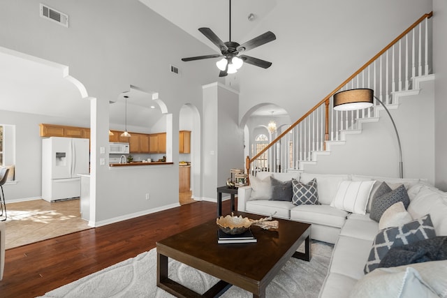 living room featuring visible vents, stairs, wood finished floors, arched walkways, and high vaulted ceiling