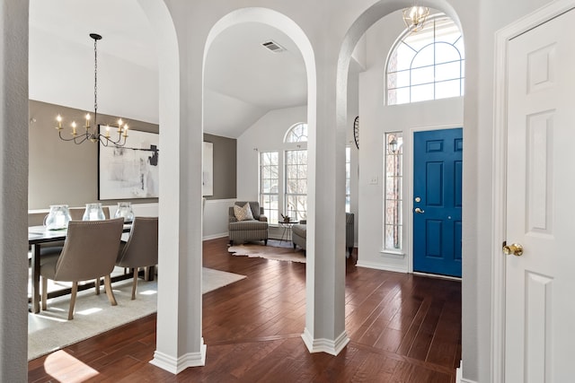 entryway featuring visible vents, arched walkways, dark wood-style flooring, vaulted ceiling, and a chandelier