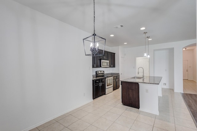 kitchen with light stone counters, appliances with stainless steel finishes, arched walkways, light tile patterned flooring, and a sink