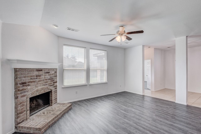 unfurnished living room with visible vents, a brick fireplace, wood finished floors, and a ceiling fan