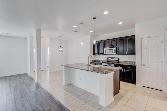 kitchen featuring dark stone countertops, visible vents, an island with sink, a sink, and appliances with stainless steel finishes