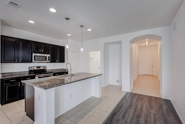 kitchen featuring visible vents, dark stone counters, dark cabinetry, stainless steel appliances, and a sink