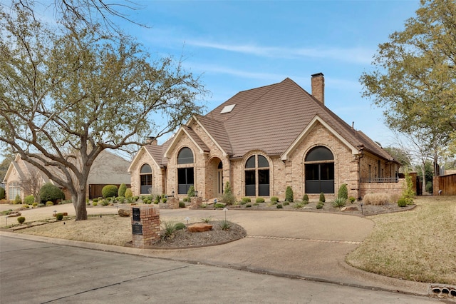 view of front of house with a tile roof, curved driveway, brick siding, and a chimney