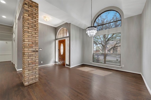 foyer with baseboards, dark wood finished floors, decorative columns, a towering ceiling, and a notable chandelier