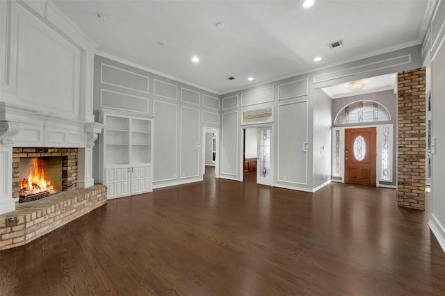 unfurnished living room with visible vents, dark wood-style floors, a decorative wall, a fireplace, and crown molding