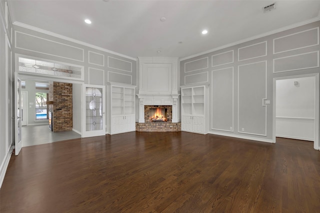 unfurnished living room with built in features, ornamental molding, a fireplace, dark wood-style floors, and a decorative wall