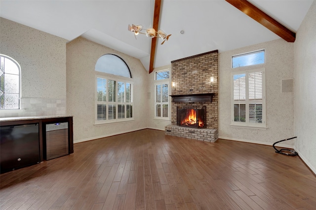 unfurnished living room featuring a wealth of natural light, beamed ceiling, high vaulted ceiling, and wood finished floors