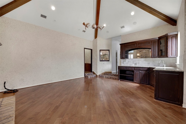 unfurnished living room with visible vents, beamed ceiling, wood finished floors, high vaulted ceiling, and a sink