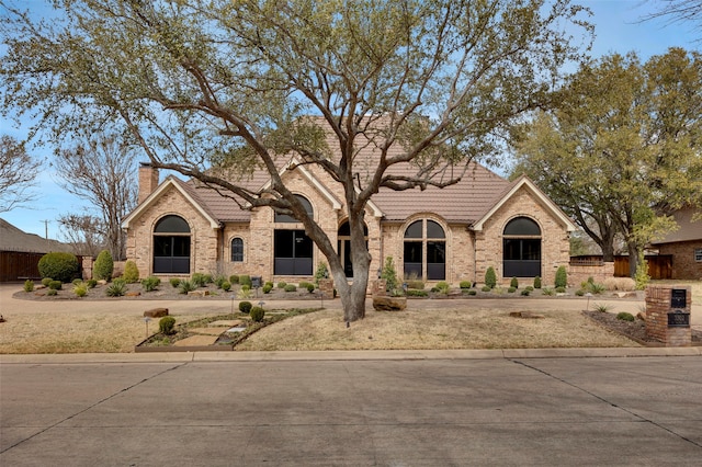 view of front of property with brick siding, a tiled roof, and a chimney