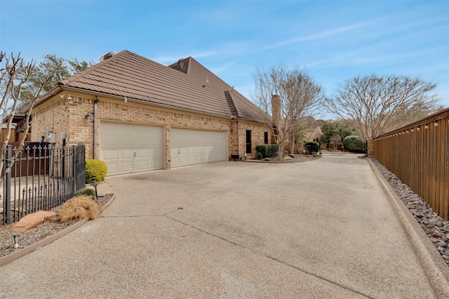 view of side of home with fence, driveway, a tile roof, and brick siding