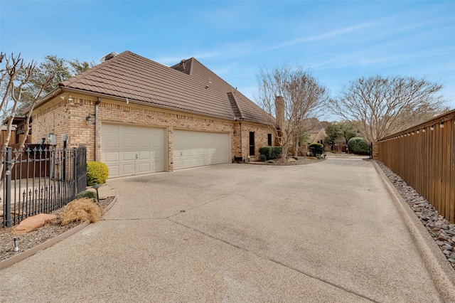 view of side of property with fence, concrete driveway, a garage, a tile roof, and brick siding