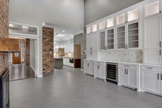 bar with pendant lighting, beverage cooler, ornamental molding, tasteful backsplash, and a towering ceiling