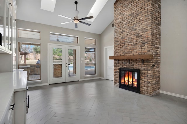 unfurnished living room with baseboards, a fireplace, a skylight, high vaulted ceiling, and a ceiling fan