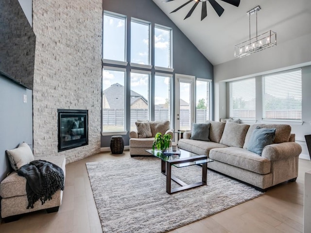 living room with high vaulted ceiling, a stone fireplace, wood finished floors, and ceiling fan with notable chandelier