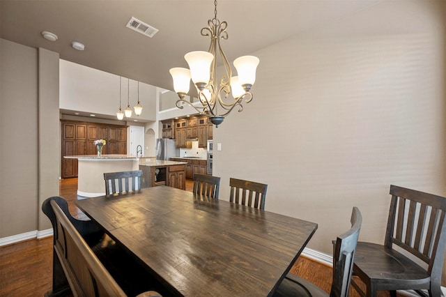 dining space with dark wood finished floors, baseboards, visible vents, and a chandelier