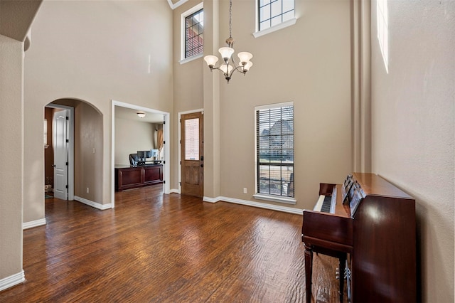 entryway featuring dark wood finished floors, arched walkways, a wealth of natural light, and an inviting chandelier