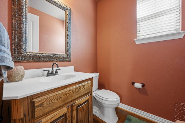 half bathroom with baseboards, toilet, wood finished floors, a textured wall, and vanity