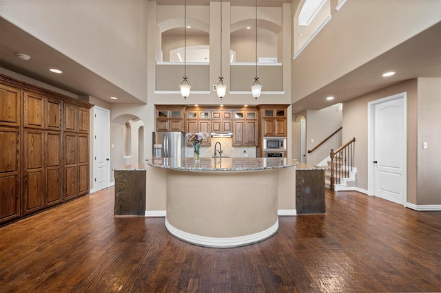 kitchen with a large island, brown cabinets, arched walkways, and stainless steel appliances