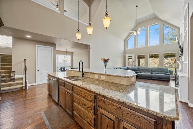 kitchen with brown cabinetry, dark wood-style flooring, ceiling fan with notable chandelier, and a sink