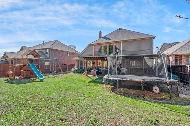 rear view of house with a playground, a trampoline, a lawn, a chimney, and a fenced backyard