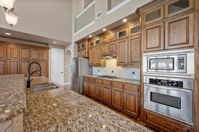 kitchen with under cabinet range hood, stainless steel appliances, brown cabinetry, and a sink