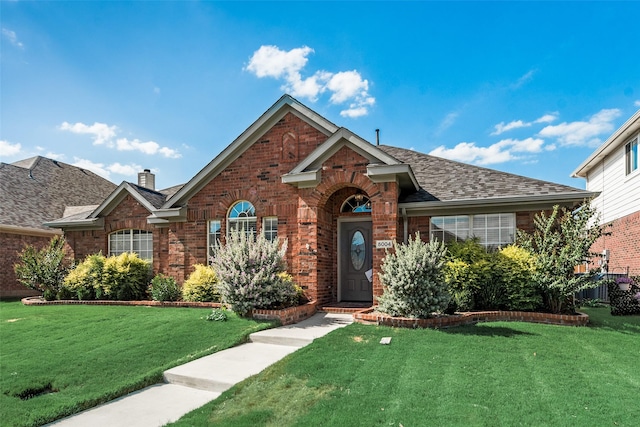 view of front facade featuring brick siding, a front yard, and roof with shingles