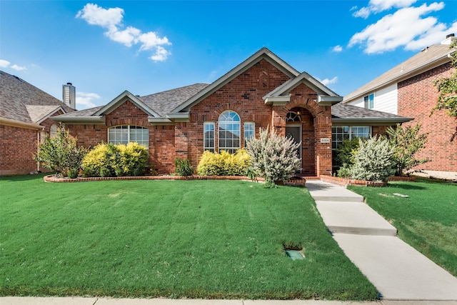 view of front of home featuring a front yard, brick siding, and a shingled roof