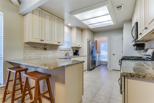 kitchen featuring visible vents, light stone countertops, a breakfast bar area, a peninsula, and stainless steel appliances