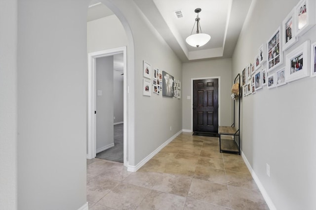 interior space featuring a raised ceiling, arched walkways, visible vents, and baseboards