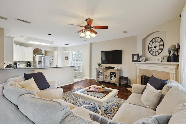 living area featuring baseboards, visible vents, a tile fireplace, ceiling fan, and dark wood-type flooring