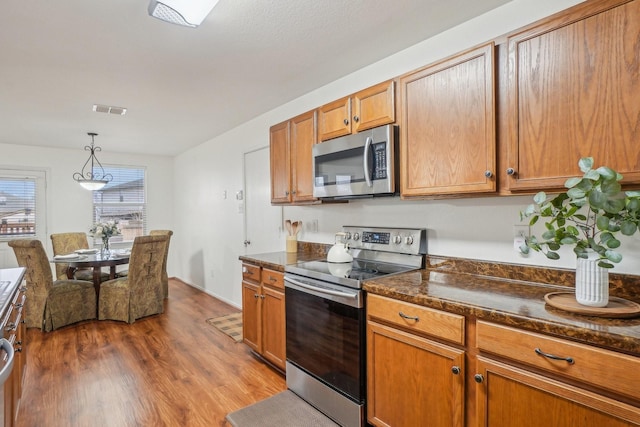 kitchen featuring dark countertops, visible vents, dark wood finished floors, brown cabinets, and appliances with stainless steel finishes