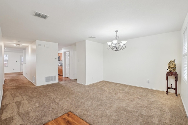 spare room with visible vents, light colored carpet, and a chandelier