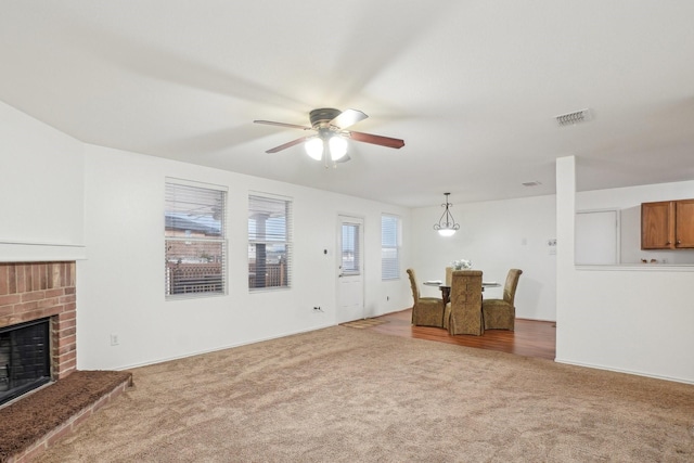 carpeted living area featuring a brick fireplace, visible vents, and ceiling fan