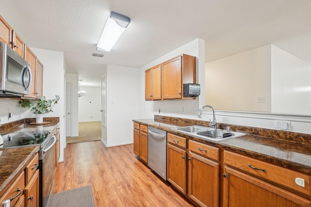 kitchen featuring light wood-type flooring, brown cabinets, a sink, dark countertops, and appliances with stainless steel finishes