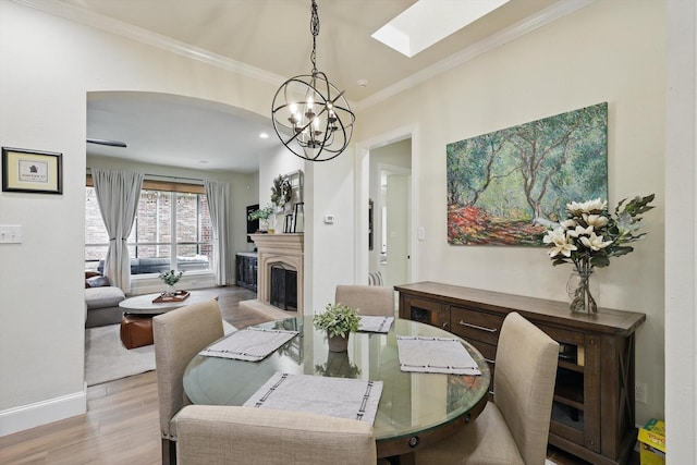 dining area featuring a notable chandelier, a fireplace with raised hearth, wood finished floors, a skylight, and crown molding