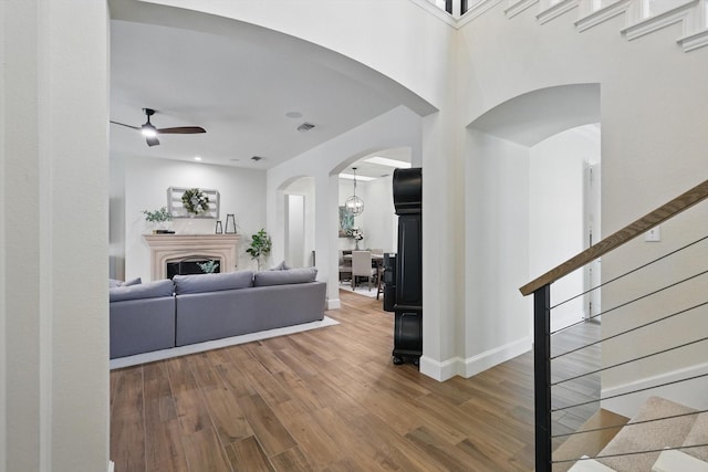 living room featuring visible vents, ceiling fan, stairway, wood finished floors, and arched walkways