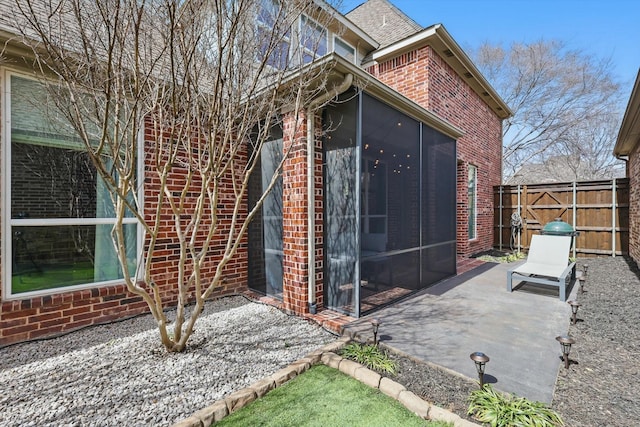 view of home's exterior with a patio area, fence, brick siding, and a sunroom