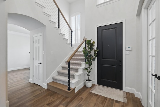 foyer with stairway, wood finished floors, arched walkways, and baseboards