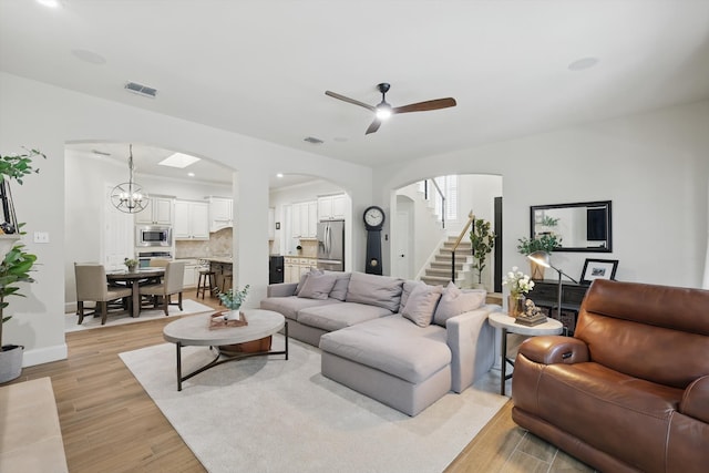 living room with stairway, arched walkways, visible vents, and light wood-style flooring