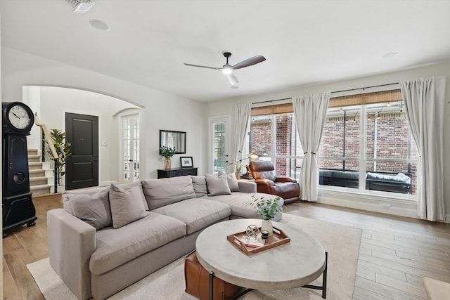 living area with light wood finished floors, visible vents, stairs, arched walkways, and a ceiling fan