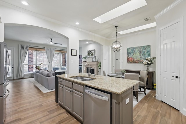 kitchen with open floor plan, dishwasher, light wood-type flooring, arched walkways, and a sink